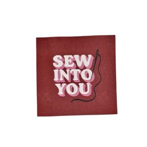 Bordeauxrode stof met geborduurd wit opschrift 'SEW INTO YOU' en naald met zwart garen